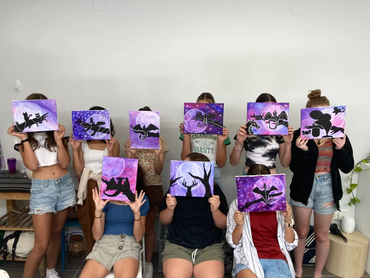 A party group holding up the moon-silhouette canvases they painted