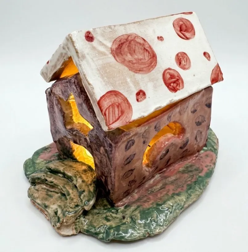 A glazed clay house with a light glowing inside, made in a ceramic clay party