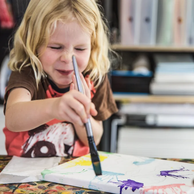 A tiny-artist painting a canvas in the studio, brush loaded with purple paint
