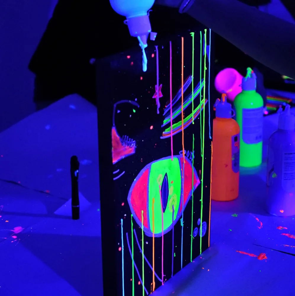 A neon painting glowing under UV light, with bright paint drips running down